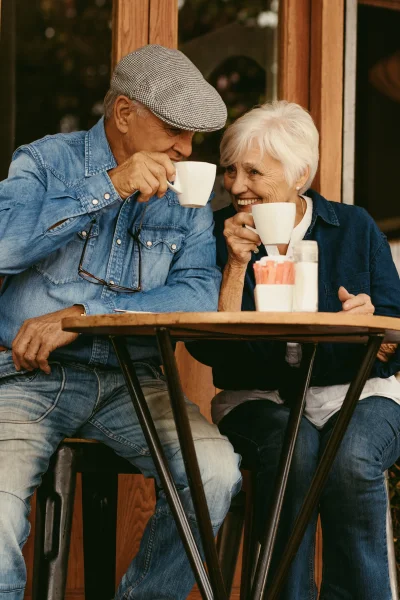 An older couple sitting at an outdoor cafe, enjoying coffee and smiling at each other.