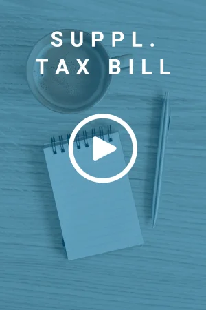 Aerial view of a cup of coffee, a pen, and an open notepad all placed on a wooden desk. There is a text overlay that reads 'Supplemental Tax Bill'.