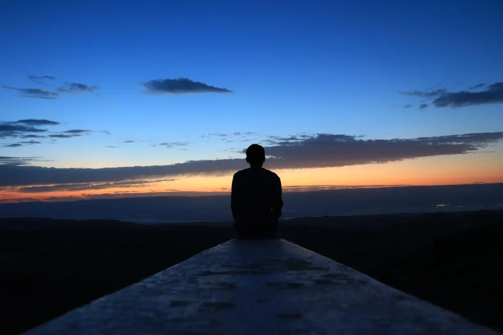 A man sits gazing at a morning sunrise over the distance.